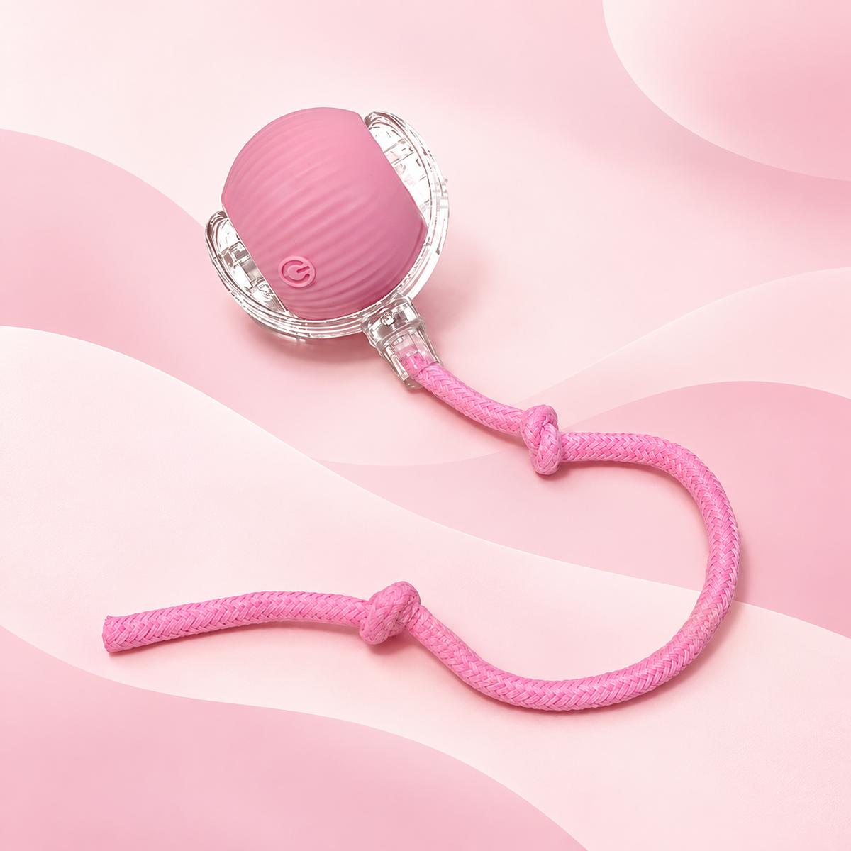 Pink Brighty MotionBall showing its power button, ribbed surface, transparent outer frame and matching knotted rope against a pink background.