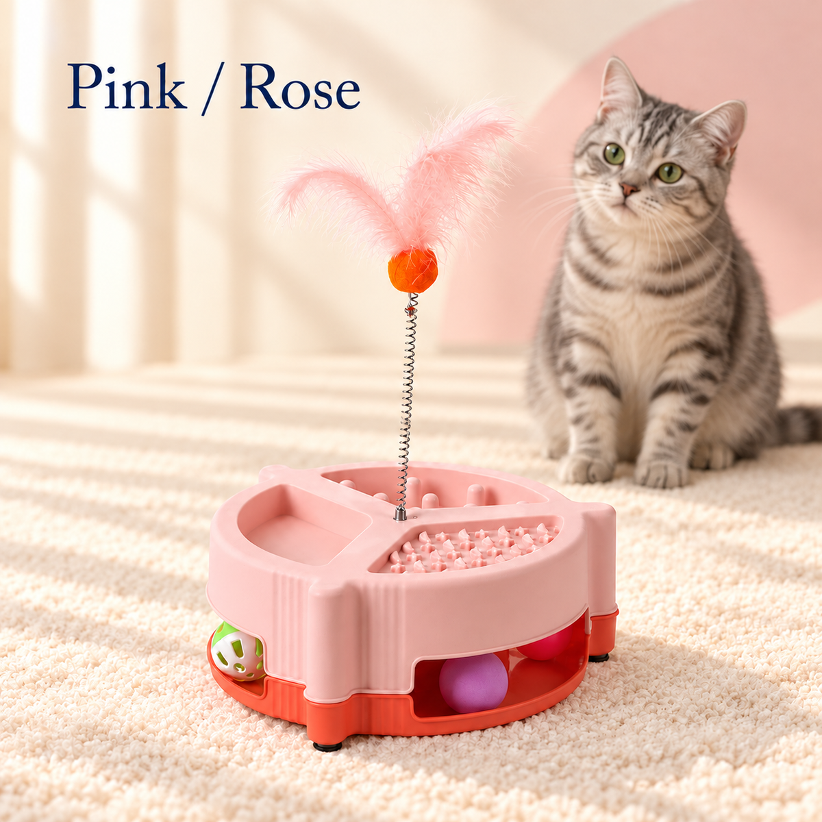 Pink Brighty MunchPlay beside a grey tabby cat, showing three feeding zones, colourful balls in the base track and pink feathers mounted on a spring.