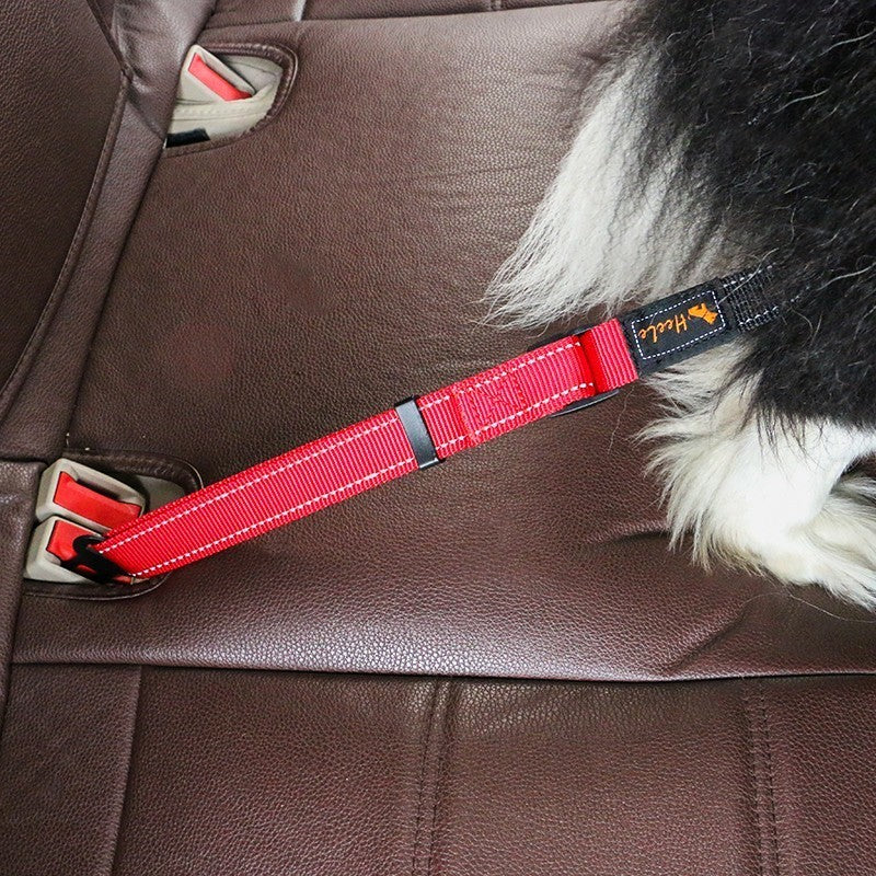 Red HEELE RoadFlex dog car tether stretched across a car seat toward a black-and-white dog, with the seat belt tab inserted into the vehicle buckle.
