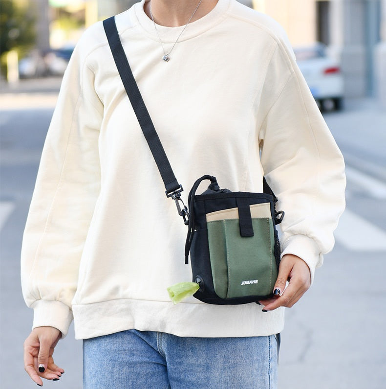 JUMAHE SnackPack dog treat bag in olive green and black, worn crossbody with adjustable strap and built-in waste bag dispenser for walks and training.
